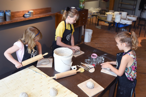 Three children working on clay projects using rolling pins, etching tools and cookie cutters.