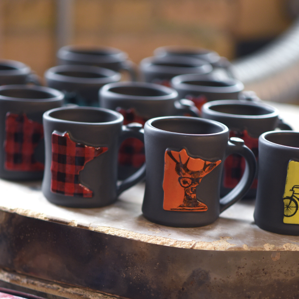 Several dark gray ceramic mugs with the state of Minnesota design in a variety of colors.