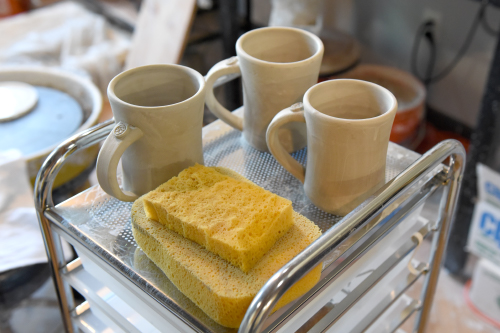 A tray with three ceramic mugs waiting to be finished and two sponges.