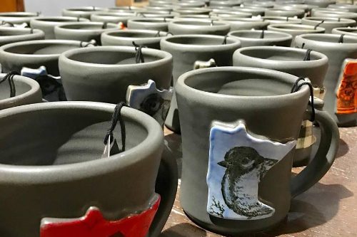 Photo of rows of black ceramic mugs with colored and printed Minnesota state decorations